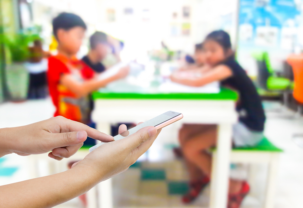 hands holding a phone with kids at table in background